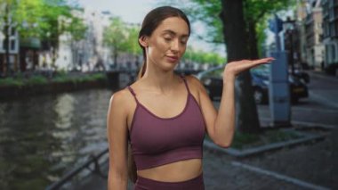 Latin kökenli genç bir kadın Amsterdam caddesinde göbeğini gösteren bir el feneri tutuyor. Mor hasat bluzu ve gün ışığında tayt giyiyor..