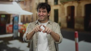 Hispanik adam şehir caddesinde parmaklarıyla kalp şekli yapıyor, içten gülümsüyor..