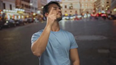 Genç İspanyol bir adam, hareketli bir şehir sokağındaki birini gece bulanık ışıklarla kovmak için jest yapıyor. Üzerinde mavi bir gömlek var. Dışarıdaki dinamik bir şehir manzarasını çağrıştırıyor..