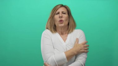 Stüdyoda yeşil arka planda titreyen bir kadın omuzlarına çapraz kollar ve büzüşmüş dudaklarıyla sarılır..