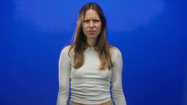 Yüzü buruşmuş genç İspanyol bir kadın, her iki orta parmağını da parlak mavi stüdyoda kameraya gösteriyor..