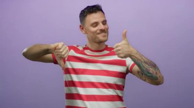 Çizgili gömlekli genç adam mor arka planda karışık baş parmaklar gösteriyor. Gülümseyerek karar verme ve değerlendirme öneriyor.