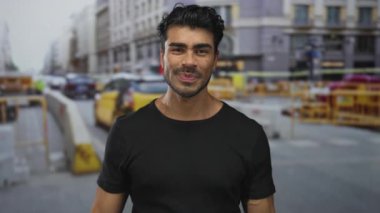 İşlek bir şehir caddesinde, sarı taksiler arasında gülümseyen ve yanakları işaret eden genç İspanyol adam; mutluluk..