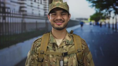 Kamuflaj üniforması giyen genç adam ve künyeler işlek şehir caddesinde güven içinde gülümsüyor..