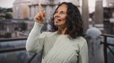 Kadın açık havada, şehirde kıvırcık saçlarıyla, şehir sokak ortamındaki pozitifliğini işaret ederek, mutluluk ve ifadesini olgun ve zarif bir şekilde sergiliyor..
