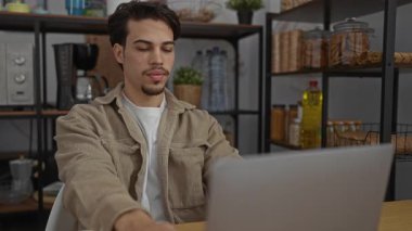 Bilgisayarın başında çalışan genç adam modern dekorasyon ve raflarla çevrili iç mekanda yemek için mola veriyor üretken bir çalışma alanı yaratıyor.