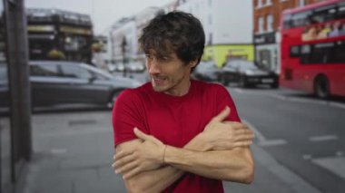 Kırmızı tişörtlü genç adam gergin bir ifadeyle ve büzüşmüş dudaklarıyla yoğun şehir caddesinde ellerini çırpıyor..