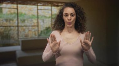 Avuç içleri açık, elleri havada ve dudakları büzüşmüş bir kadın oturma odasının içinde..