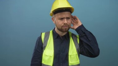 Stüdyoda el ele tutuşan sarı şapkalı ve yansıtıcı yelekli adam; güvenlik farkındalığı mavisi.