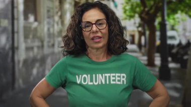 Orta yaşlı, çapraz kollu bir kadın gönüllü üniforma ve gözlük takarak bir ağaçta duruyor. Reddedilmeyi reddediyor..