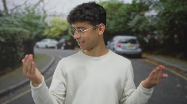 Gözlüklü genç İspanyol adam, avucunu incelerken park halindeki arabaların önünde ellerini kaldırır..