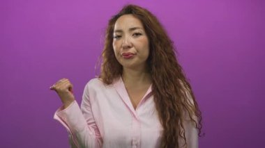 Stüdyoda pembe gömlekli bir kadın mor duvara başparmağıyla işaret ediyor, şüphecilik reddediliyor..