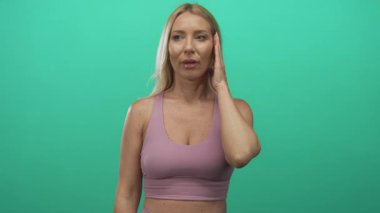 Spor sutyen giyen bir kadın yeşil duvara el ele tutuşarak yanağa dokunuyor; diş ağrısı rahatsızlığı.