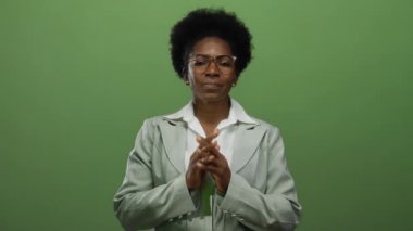 Gözlüklü ve takım elbiseli kadın, elleri izole edilmiş yeşil bir zemine kenetlenmiş, sakin bir şekilde duruyor..