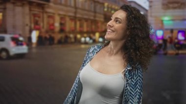 İki parmakla gülümseyen ve işaret eden bir kadın, alacakaranlıkta bir şehir caddesinde görünür bir omuz; neşe.