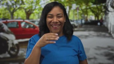 Mavi gömlekli kadın, gün ışığında şehir caddesinde el hareketleriyle ağzını kapatıyor..