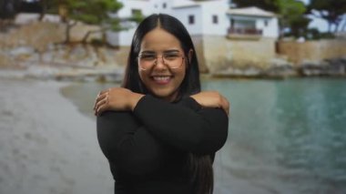 Kadın plaj zeminine sarılarak kollarını sarıyor. Deniz kenarında Latin asıllı genç bir kız usulca gülümsüyor..