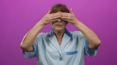 Elleri gözlerinin üzerinde olan bir kadın, onları kaldırır, ve şaşırır, canlı pembe bir arka plan karşısında, yaşlı bir İspanyol temizlikçi için neşeli, beklenmedik bir an yaşatıyor..