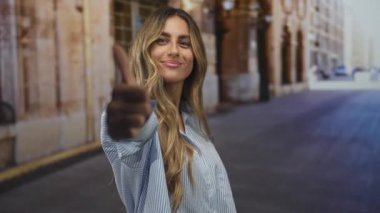 Sarışın genç kadın, güneş ışığıyla aydınlanan kaldırım taşı sokakta olumlu bir jest yapıyor. Onaylanan güven iyimserliği.