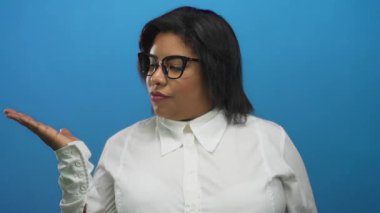 Beyaz gömlekli ve gözlüklü, iri yarı, İspanyol bir kadın, mavi duvarın üzerinde yüz ifadesiyle el ele tutuşuyor..