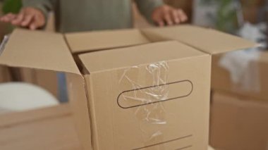 Adam nazikçe ellerini bir binanın içindeki bantlanmış bir karton kutuyu açmak için kullanır; yeni bir başlangıç iyimserliği.