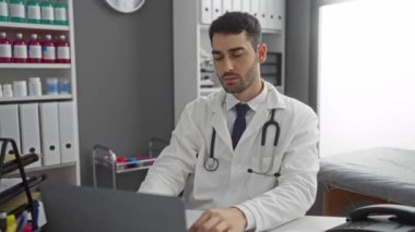 İspanyol erkek doktor, bir klinikte dizüstü bilgisayara odaklanmıştı. Gündüzleri ensesinde tıbbi malzeme rafları ve steteskop vardı..