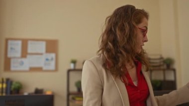 Ofisteki kadın, kitaplarla ve bitkilerle çevrili raflarla çevrili gözlük ve kırmızı tişört takarak ev içi profesyonel ortamlarda canlı iletişim kuruyor..