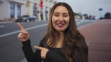 Genç İspanyol kadın şehir binasının önündeki caddeyi işaret ediyor. Gözleri yukarı bakıyor. Meraklı bir keşif..