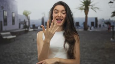 Gülümseyen genç İspanyol kadın, parlak bir sabahta palmiye ağaçlarının altında sokakta beş parmak sayıyor..