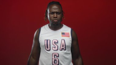 ABD basketbol forması giyen bir adam stüdyoda kırmızı arka planla parmaklarını kulaklarına tıkıyor..