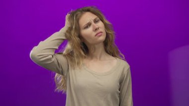 Stüdyoda kafasını kaşıyan bir kadın sarışın, genç, kafası karışık mor arka plan portresiyle yakalandı..