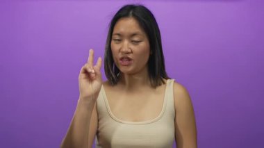 İzole edilmiş mor arka plana karşı çeşitli duygular beyan eden bir kadın kolsuz tişörtlü genç Çinli bir kadın renkli duvarın üzerinde yüz ifadeleri ve jestler sergiliyor..