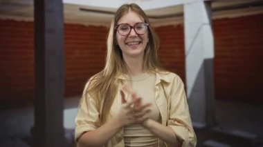 Genç, sarışın, gözlüklü, gülümseyen ve elini sıkan bir kadın..