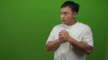 Genç Çinli adam gergin bir ifadeyle yeşil stüdyo duvarının önünde el sıkışıyor..
