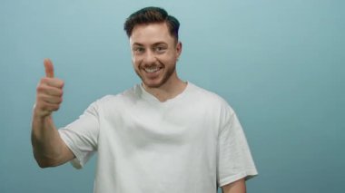 Parmakla gülümseyen genç bir adam canlı mavi bir arka plana karşı bir jest, izole edilmiş bir stüdyo ortamında pozitiflik ve güven yayıyor.