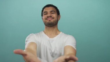 Gülümseyen adam turkuaz stüdyoda çıplak ellerini uzatarak doğrudan bakış hareketi sunuyor; hoş geldin bağlantı desteği güven.