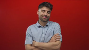 Kırmızı stüdyo ortamında kameraya hafifçe gülümseyen kolları çapraz ve kolları çıplak bir adam, sakin güven.