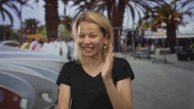 Sarışın kadın, meşgul caddede palmiye ağaçlarıyla kaplı kamerayı işaret ederken çıplak yanağını eliyle kapatıyor..