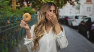 Kadın bir eliyle donut tutuyor, diğer eliyle şehir sokağında burnunu sıkıyor, mide bulantısı, reddetme tiksintisi..