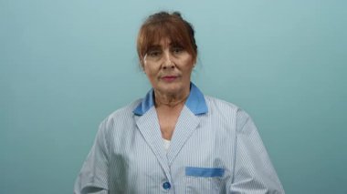 Mavi bir duvar arkasında izole edilmiş düşünceli bir ifadeyle kıdemli İspanyol kadın, iç ve profesyonel bir atmosfer sergiliyor..