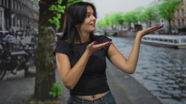 Kadın ellerini açarken gülümser ve siyah bluz giyerken avuçlarını kaldırır; davetiye.