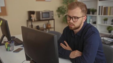 Ofis binasında bilgisayar monitöründe, gözlüklü ve kolları katlanmış bir şekilde oturan bir adam, yorgunluk verimliliği.