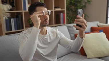 Modern apartman dairesinde selfie çeken adam, camları çıkarıyor, akıllı telefon kullanıyor, rahat atmosfer kullanıyor, kapalı mekanda, doğal ışık, ev dekorasyonu, rahat iç mekan..