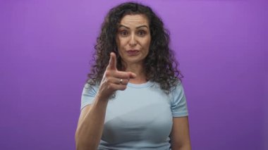 Açık mavi tişörtlü, ciddi bir ifadeyle parmağı olan ve mor stüdyoya dik dik bakan genç İspanyol kadın..