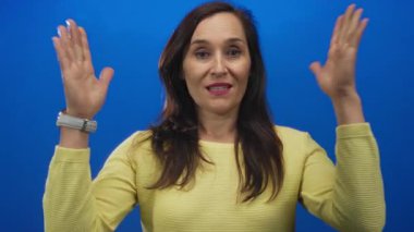 Latin kökenli genç bir kadın mavi bir stüdyoda büyük bir jest yaparak el ele tutuşuyor..