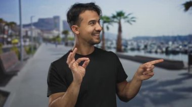 Deniz kıyısındaki genç adam, neşeli bir gülümsemeyle, uzaklığı gösteren, temiz bir gökyüzünün altında palmiye ağaçları ve kayıklar tarafından çerçevelenmiş,.