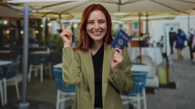 Kızıl saçlı kadın Kore pasaportunu şehir terasında tutuyor gülümsüyor ve yeşil ceket giyiyor..