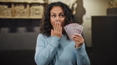 Müzede Meksika pezosu tutan kadın, tarihi geçmişi ve duyguları vurgulayan mavi bir süveter giydiğine şaşırmış görünüyor..