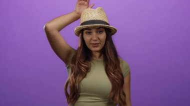 Şapka takan İspanyol kadın, neşeli kulaklar yapıyor. Canlı mor duvarlara karşı elleri ile, izole bir ortamda neşe ve mizah gösterisi yapıyor..