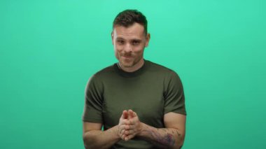 Dövmeleri olan genç bir adam, izole edilmiş yeşil bir arka plana karşı jest yapar.